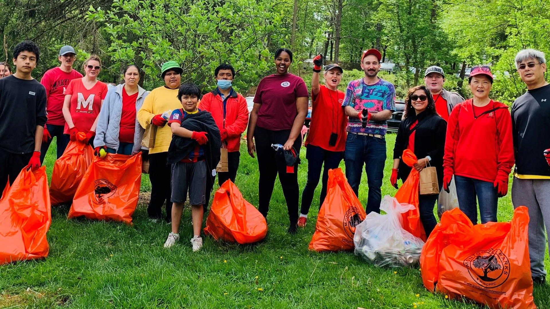 A group of volunteers are posing, smiling with bags of trash they cleaned up from a local park.