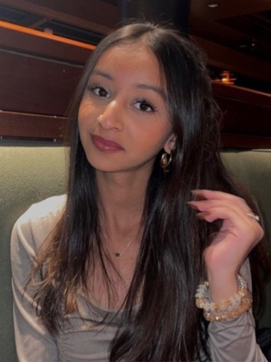 Rida's headshot is a woman with black hair sitting in a sage green chair. She is wearing a grey shirt. 