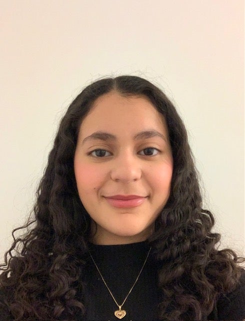 Ayan Hamouda's headshot features her smiling with long black hair in a black top.