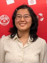 Annie Song's headshot features Annie with short black and hair and glasses in front of a red background with white icons on it. 