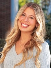 Ella Coopers headshot. A young blonde woman smiles in front of a blurry background.