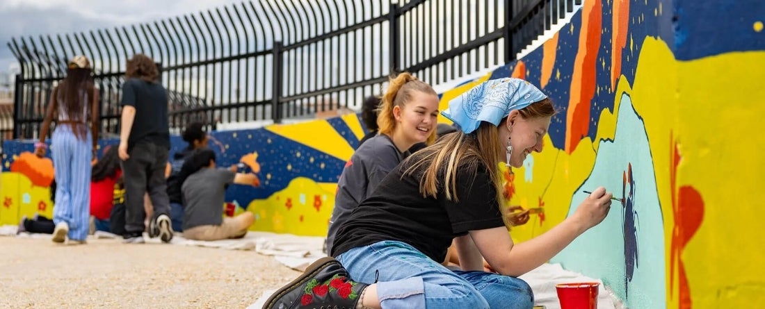 students painting blue and yellow mural on top of a parking garage