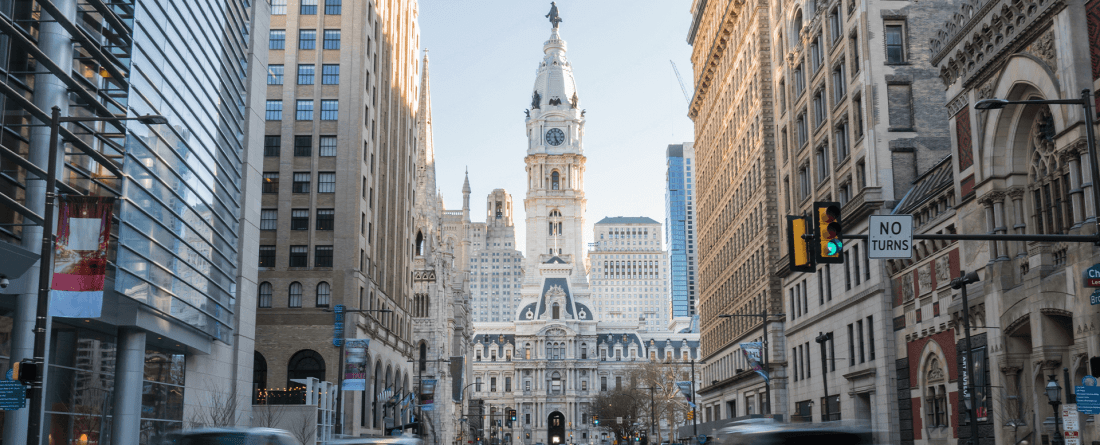 A view of a tall historic building surrounded by modern structures with cars driving through the street.