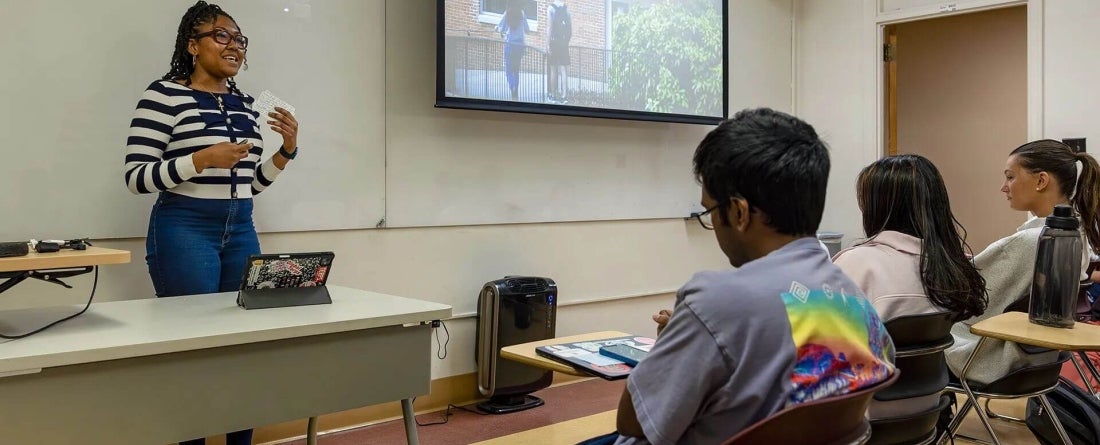 student standing in front of Comm107 class full of students